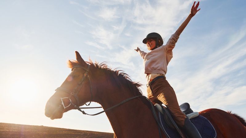 Eine junge Frau sitzt auf einem Pferd und breitet ihre Arme aus.