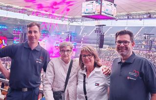 Zwei Helfer der Malteser und zwei Frauen stehen als Zuschauer bei einem Konzert