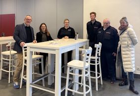 Sechs Personen stehen um einen Stehtisch herum und blicken in die Kamera