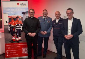 Lucas Weiss, Boris Falkenberg, Claus Kemp und Carsten Braun stehen vor einer Wand neben einem Banner auf dem Neujahrsempfang der Malteser