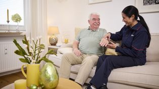Eine Hausnotruf Mitarbeiterin legt einem Senioren ein Hausnotrufarmband an