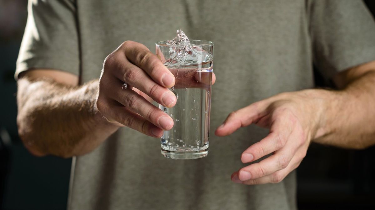 Ein Mann hält ein Wasserglas, das überschwappt.