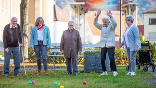 Eine Gruppe älterer und jüngerer Menschen spielt auf einer Wiese Boccia.