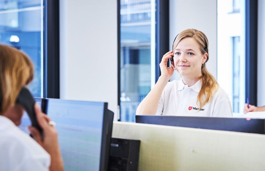 Eine junge Frau steht hinter ihrem Computer und telefoniert über ein Headset