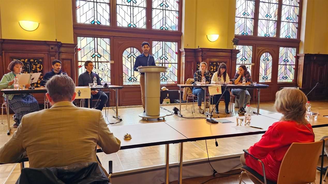 Junge Menschen auf einer Bühne vor einer Jury bei einer Debatte.