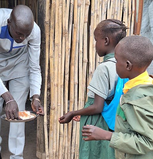 Ein Mann aus dem südsudan verteilt Essen an zwei Kinder