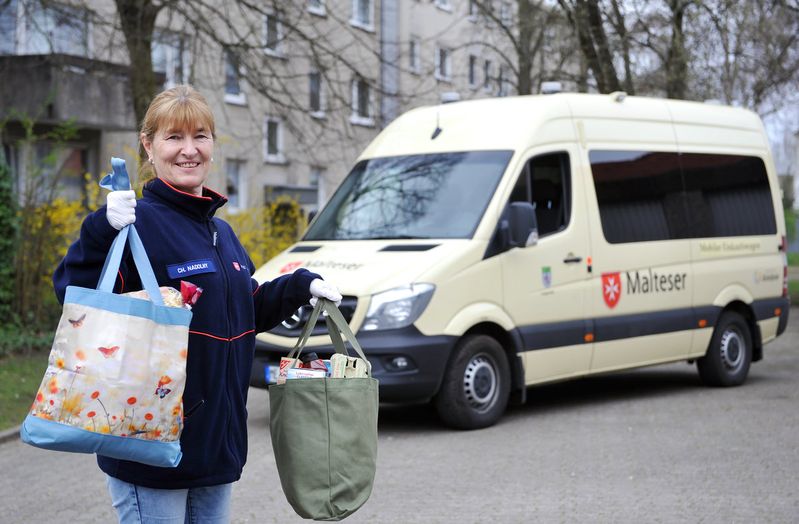 Frau mit Einkaufstaschen vor einem Fahrzeug der Malteser