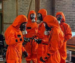 Malteser Ehrenamtliche üben Handbewegungen in Schutzanzügen beim CBRN-Grundlehrgang.