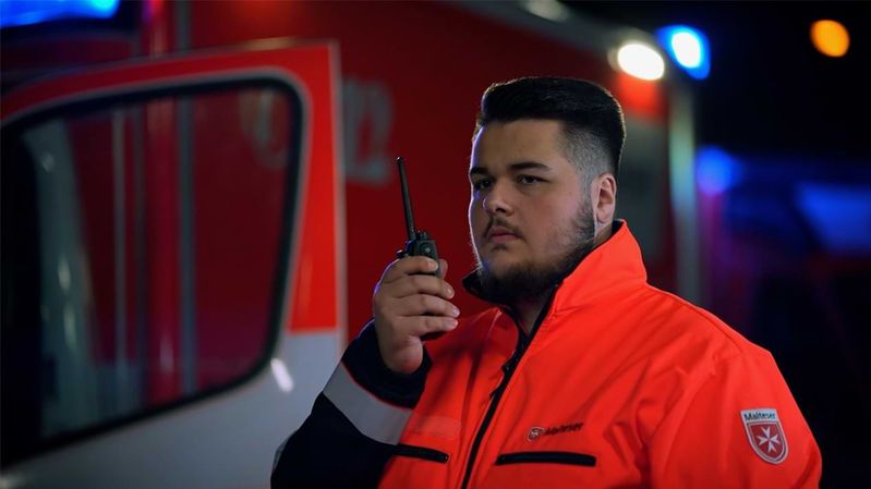 Ein junger Mann in Einsatzkleidung der Malteser mit einem Funkgerät in der Hand.