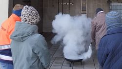 Ein Mann löscht ein Feuer in einer Feuerschale, während ein Malteser Ausbilder und weitere Kursteilnehmende zuschauen.