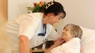 Pflegerin hilft einer alten Frau im Krankenhausbett.