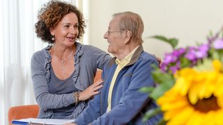 Eine Frau unterhält sich mit einem älteren Mann und legt ihm den Arm um die Schultern.
