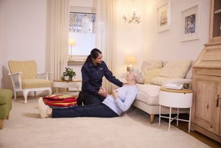 Frau mit grauen Haaren sitzt zeitunglesend auf einem hellgrauen Sofa