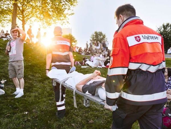 Zwei Sanitäter tragen eine Patientin auf einer Trage während einer Veranstaltung im Freien.