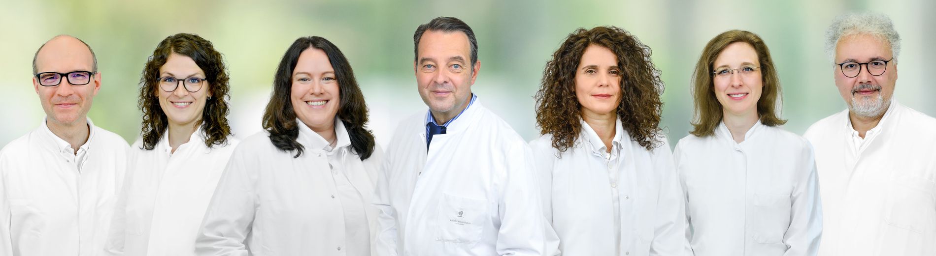 Sieben medizinische Fachkräfte der Klinik für Akutgeriatrie und geriatrische Rehabilitation in weißen Kitteln stehen nebeneinander.