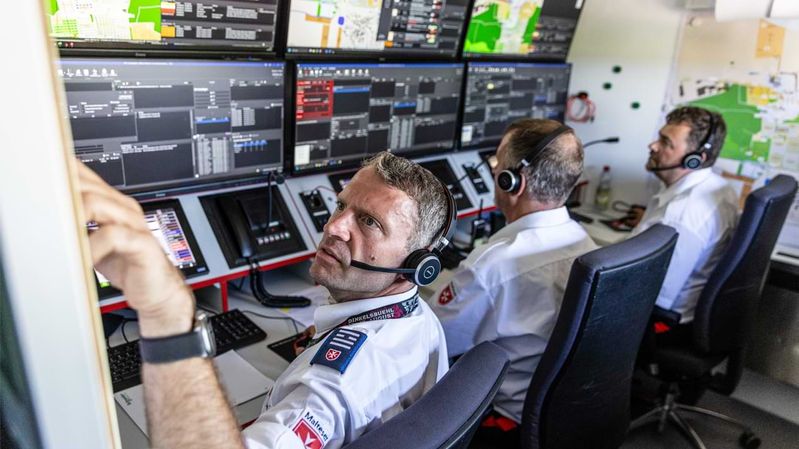 Drei Männer sitzen vor Monitoren und tragen dabei Headsets.