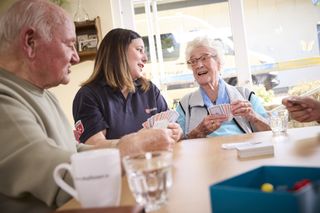 Malteser Ehrenamtliche spielt Karten mit zwei älteren Menschen
