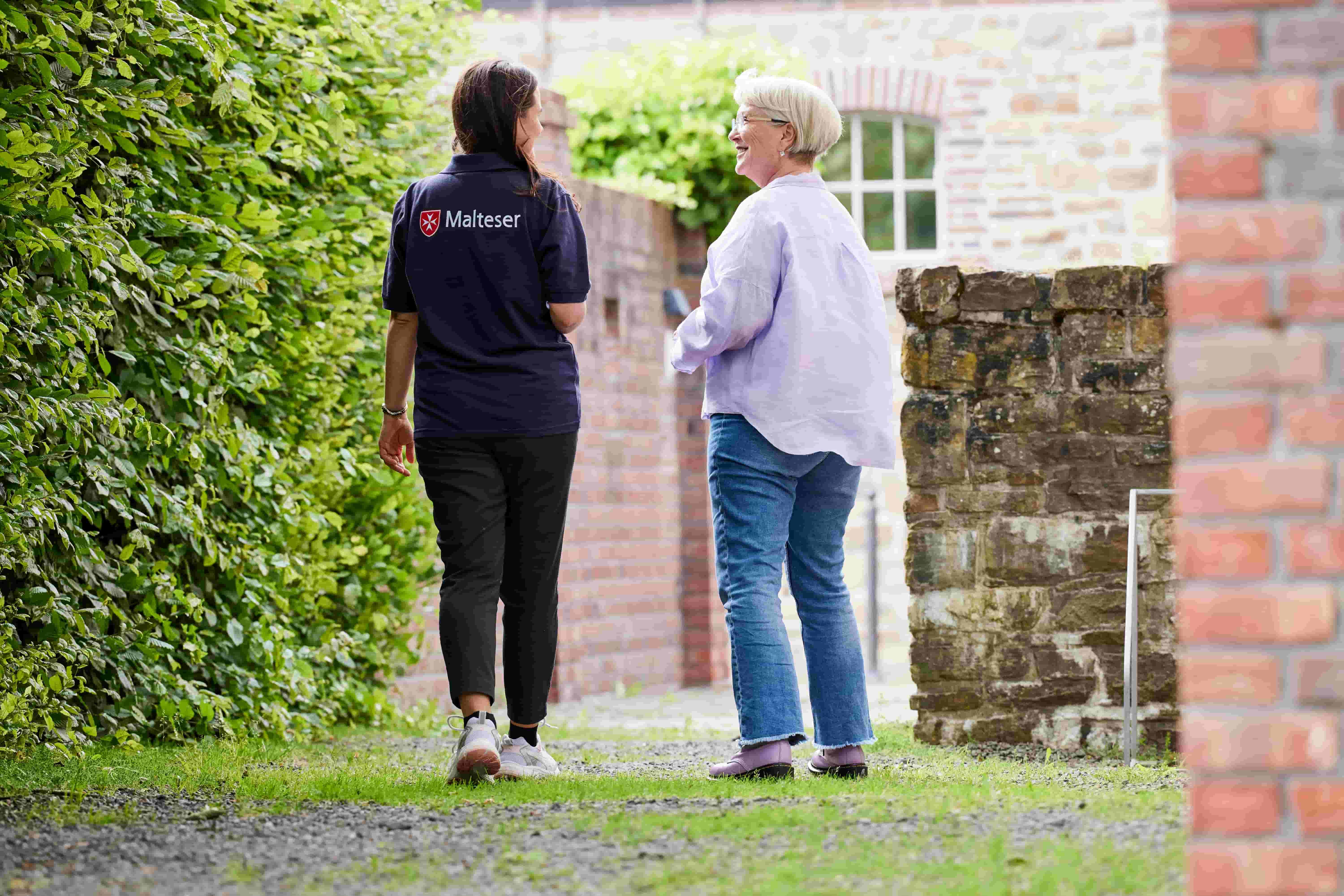 Eine Malteser Mitarbeiterin spaziert mit einer älteren Frau.