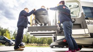 Zwei Mitarbeitende des Malteser Fahrdienstes helfen einer Person im Rollstuhl.