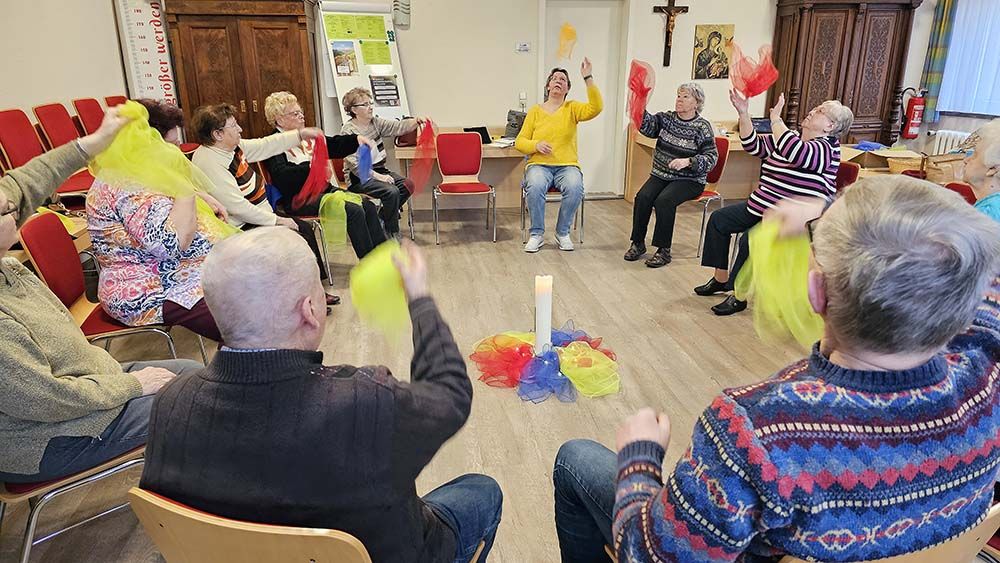 Männer und Frauen sitzen auf Stühlen, die in einem Kreis stehen. Sie bewegen sich auf den Stühlen.