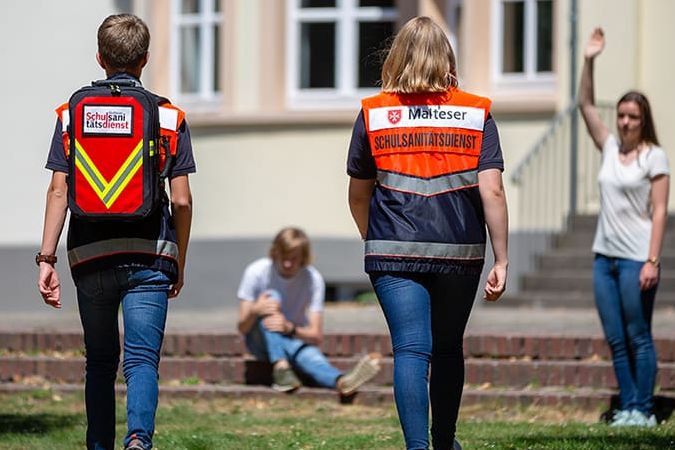 Zwei Schulsanitäter eilen zu einem verletzten Schüler auf dem Schulhof.