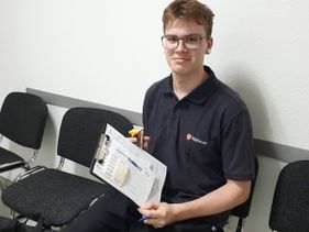 Ein junge Mann hält ein Klemmbrett mit Papier fest.