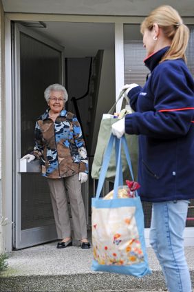 Malteser-Ehrenamtliche übergibt Seniorin Einkäufe.