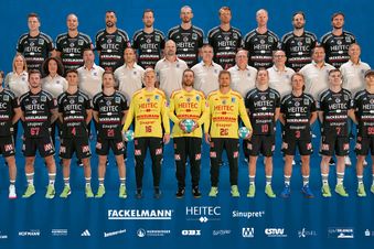 Teamfoto des Handballclubs HC Erlangen mit Spielern in schwarzen Trikots und Betreuern in weißen Shirts.