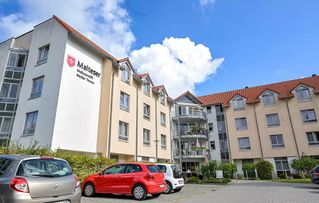 Ein Mehrfamilienhaus mit dem Malteser-Logo und geparkten Autos im Innenhof.