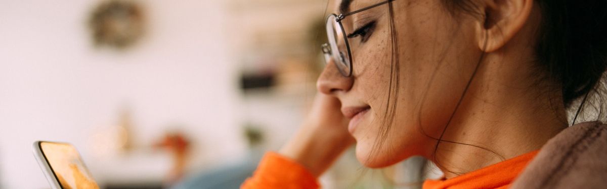 Junge Frau mit Brille schaut auf ein Smartphone.