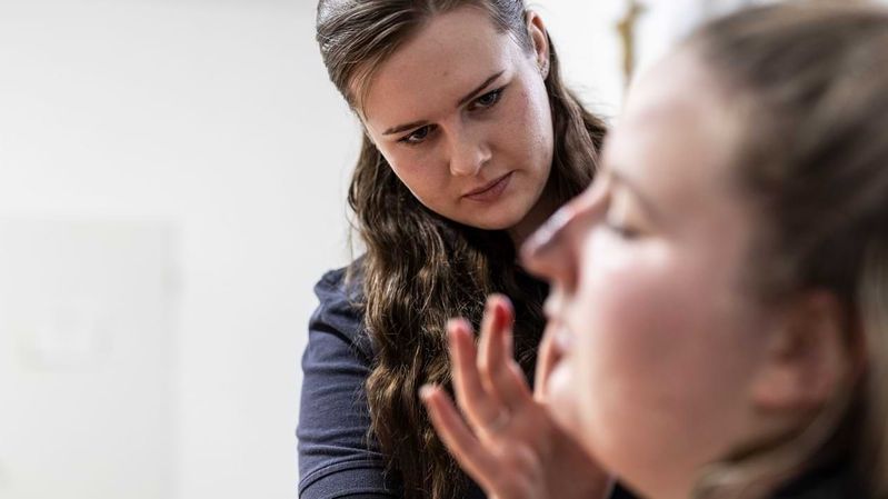 Eine junge Frau schminkt einer anderen eine täuschend echte Wunde ins Gesicht.