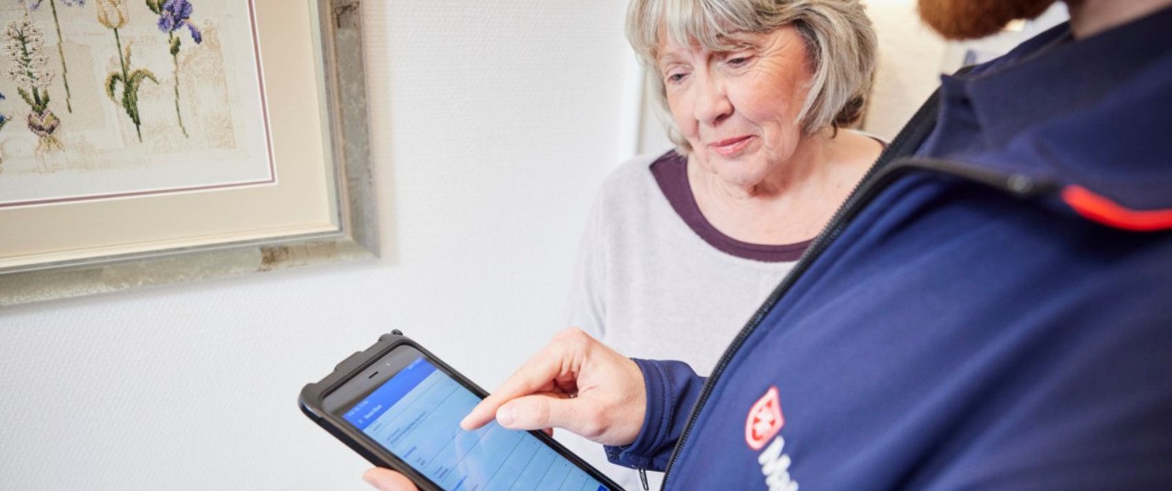 Seniorin schaut sich mit einem Hausnotrufmitarbeiter einen Vertrag über ein Tablet an