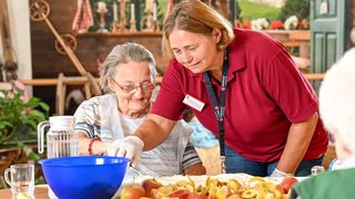 Eine Betreuungskraft der Malteser hilft einer älteren Frau dabei, Äpfel zu schneiden