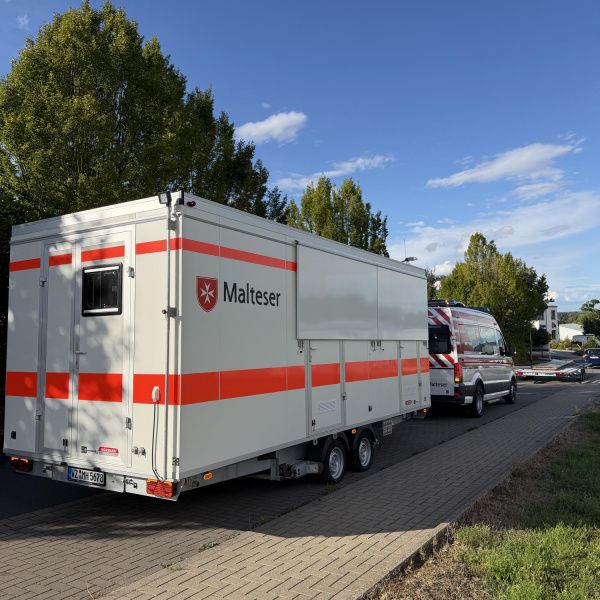 Die Malteser-Sanitätsstation bestehend aus einem Bus und einem Anhänger stehen an einer Straße von hinten fotografiert.