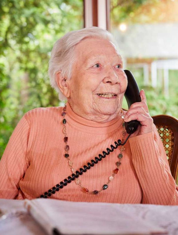 Eine ältere Dame sitzt am Tisch und telefoniert.