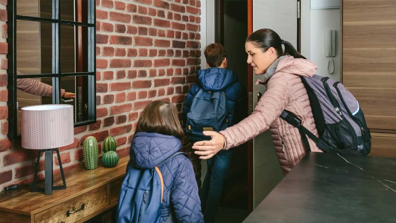 Eine Frau und zwei Kinder mit Rucksäcken verlassen eine Wohnung.