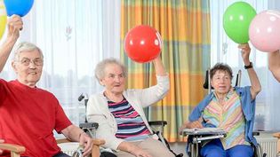 Ältere Menschen halten einen Luftballon in die Luft.