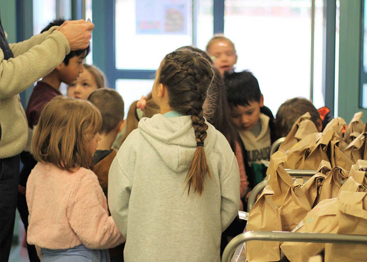 Kinder stehen vor einem Rollwagen mit Papiertüten.