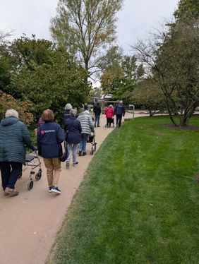 Die Malteser begleiten eine Gruppe mit Rollatoren durch den Park
