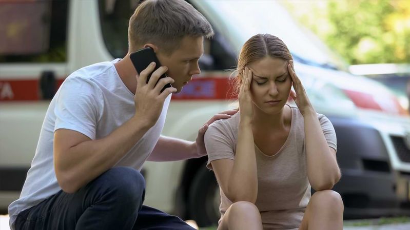 Ein Mann mit Smartphone am Ohr kümmert sich um eine Frau, die auf der Straße sitzt.