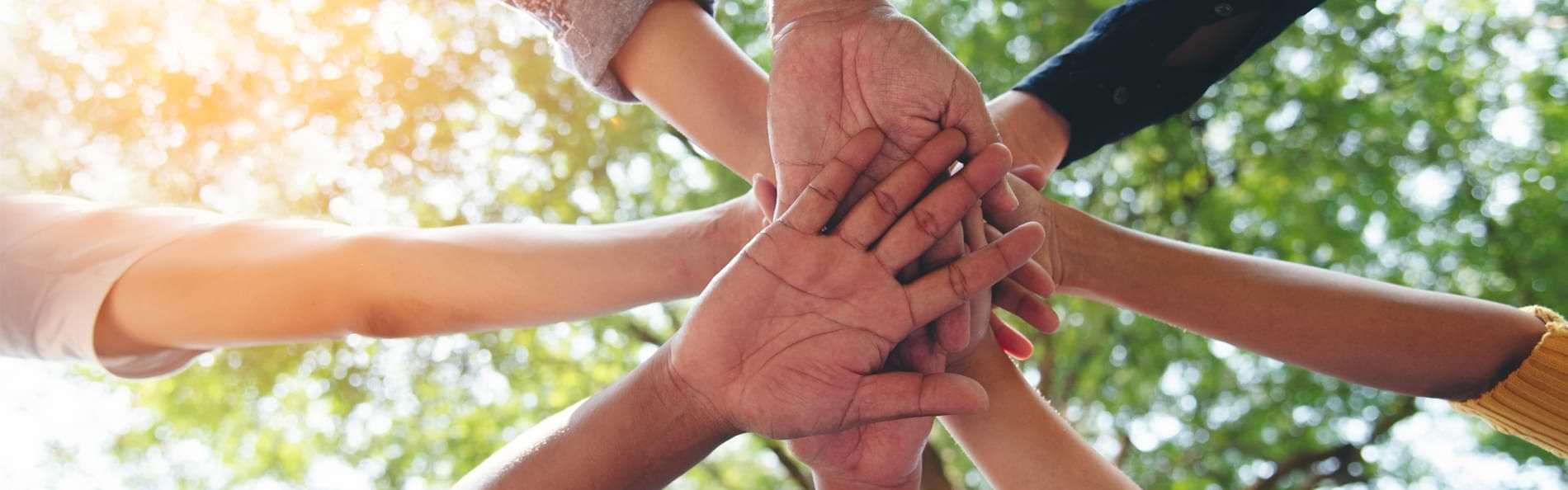 Zusammengelegte Hände mehrerer Menschen von unten fotografiert.