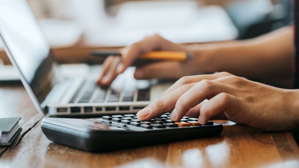 Hände halten einen Stift und tippen auf Laptop und Taschenrechner