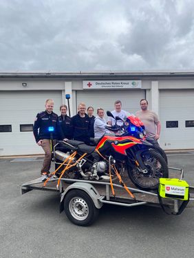 Gruppenfoto: Die Teilnehmenden des Fortbildungswochenendes mit zwei Motorrädern auf einem Anhänger