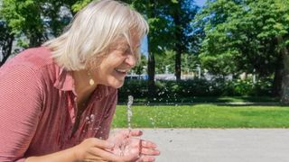 Ältere Frau erfrischt sich an einem Brunnen
