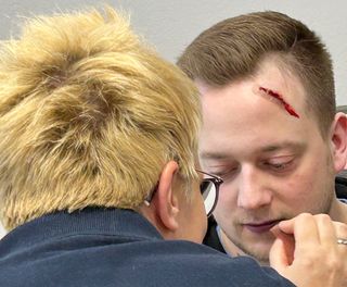 Realistische Unfalldarstellung: Eine Malteser Helferin schminkt einem Laienschauspieler realistisch wirkende Verletzungen am Kopf