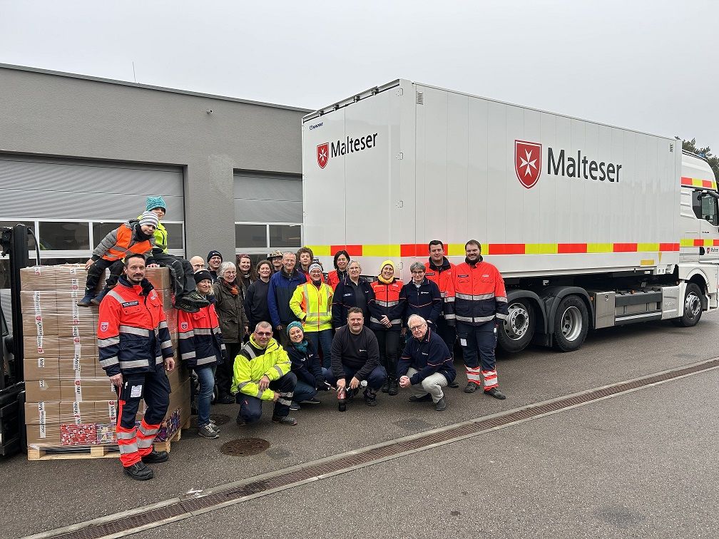 Viele Menschen in Einsatzkleidung mit einer Palette voll Pakete vor einem Malteser Lkw