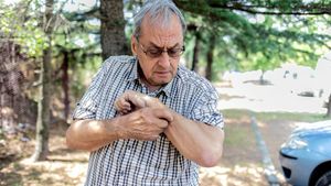 Ein älterer Mann mit Brille und kurzem Hemd kratzt sich am linken Arm.