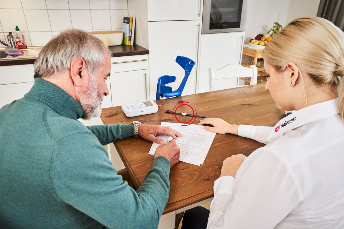 Mitarbeiterin der Malteser hilft einem Senior bei der Hausnotruf Vertragsabwicklung.