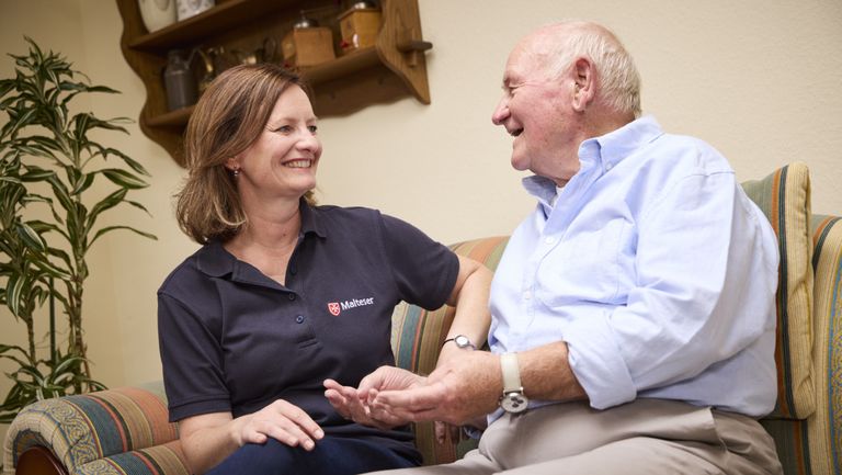 Eine lächelnde Frau und ein älterer Mann sitzen auf einem Sofa und unterhalten sich.