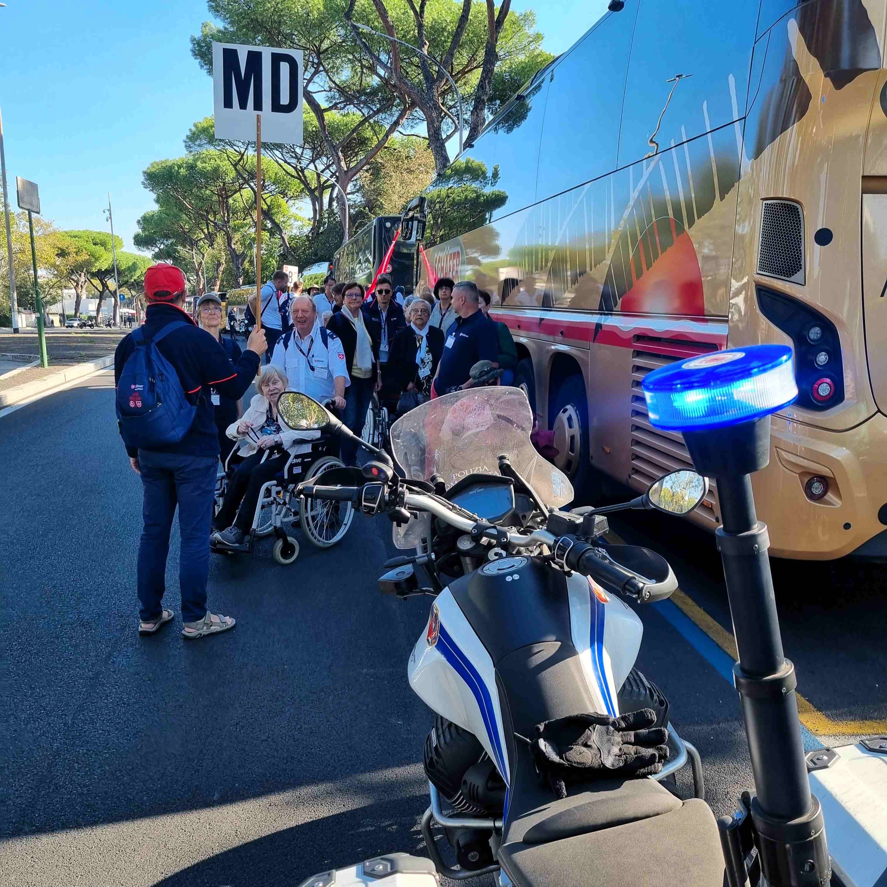 Motorrad mit eingeschaltetem Blaulicht steht an Straßenrand, dahinter Menschen und ein Bus mit geöffneter Tür.